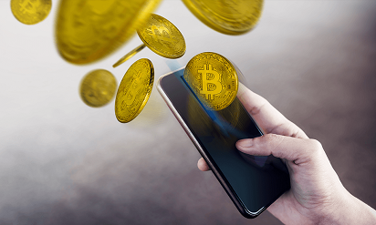 A hand holding a smart phone showing an explosion of Bitcoins, with a dark grey background.