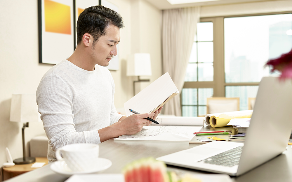 A guy analyzing financial market graph and preparing a trading plan, holding a notebook and pen, and a laptop in front of him.