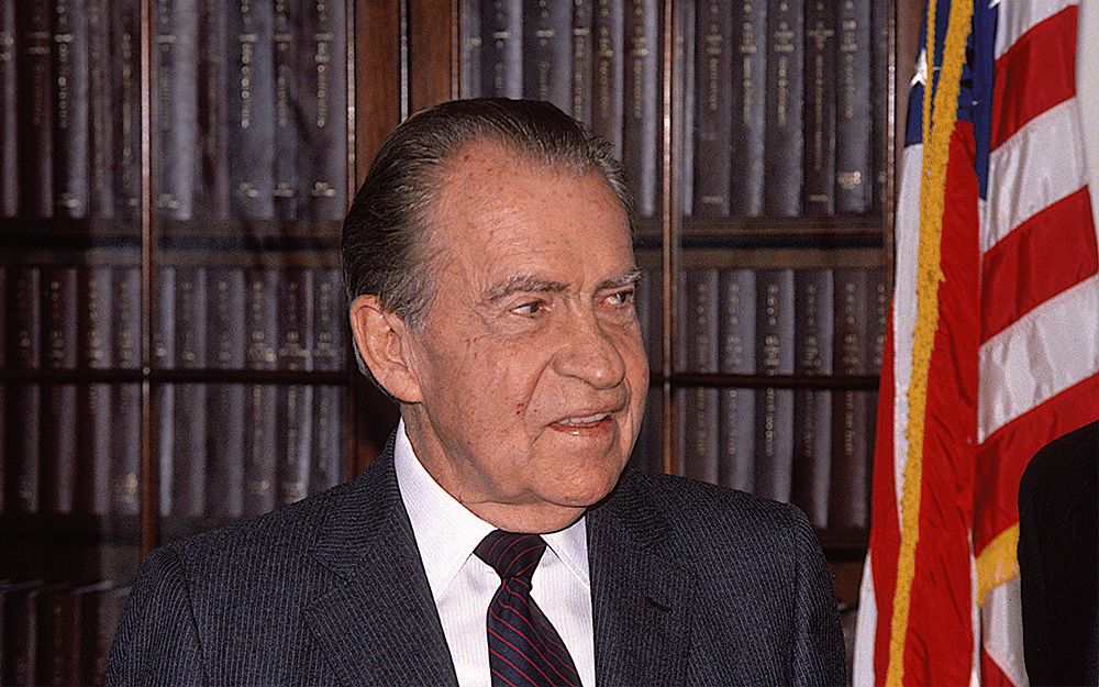 The ex-president of USA, Richard Nixon, standing beside the flag of USA.