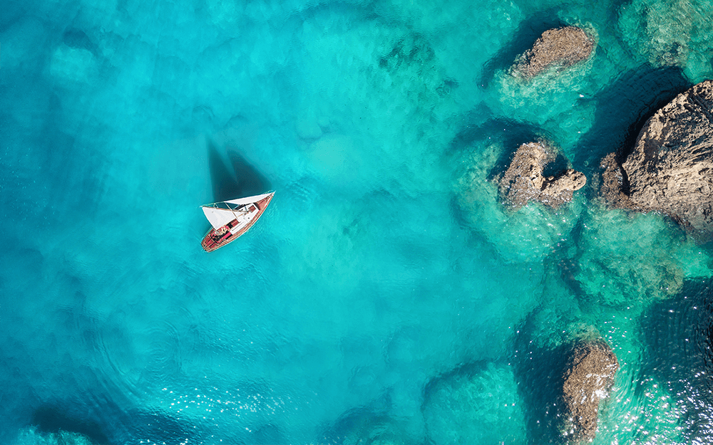A small boat sailing on a turquoise-colored sea reflecting its shadow in the water.